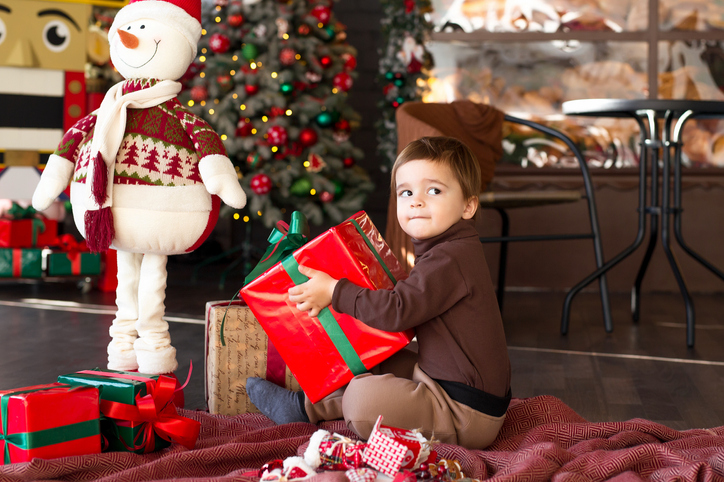 Cute toddler boy with red Christmas present at home close-up. New Year's comfort at home.