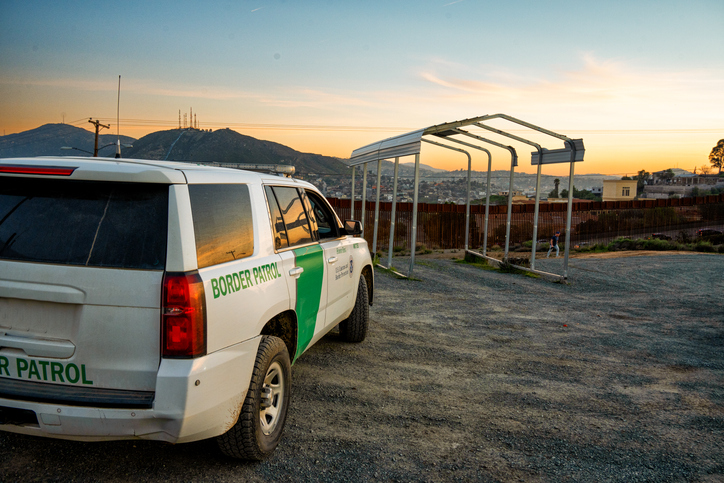 U.S. Border Patrol Official Vehicle Parked Near the International Border Barrier Wall Between the United States and Mexico in Tecate California at Dusk With Pretty Cloudscape