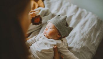 Mother holding cute baby boy wearing wooly crown on bed at home