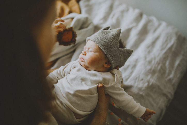 Mother holding cute baby boy wearing wooly crown on bed at home