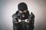 a bandit in black mask and gloves with handcuffs in his hands on a white background. Release from imprisonment. an evil thief is trying to break the chain on the handcuffs.
