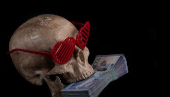Model of a human skull in sunglasses in the shape of a human heart symbol and a stack of banknotes in denominations of 10,000 Kazakhstani tenge