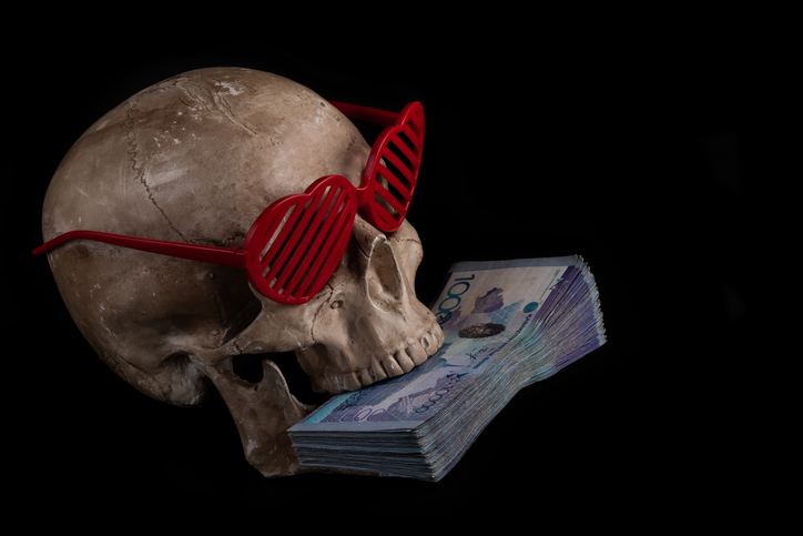 Model of a human skull in sunglasses in the shape of a human heart symbol and a stack of banknotes in denominations of 10,000 Kazakhstani tenge