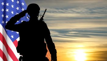Silhouette of a saluting soldier with USA flag against the sunset