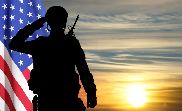 Silhouette of a saluting soldier with USA flag against the sunset