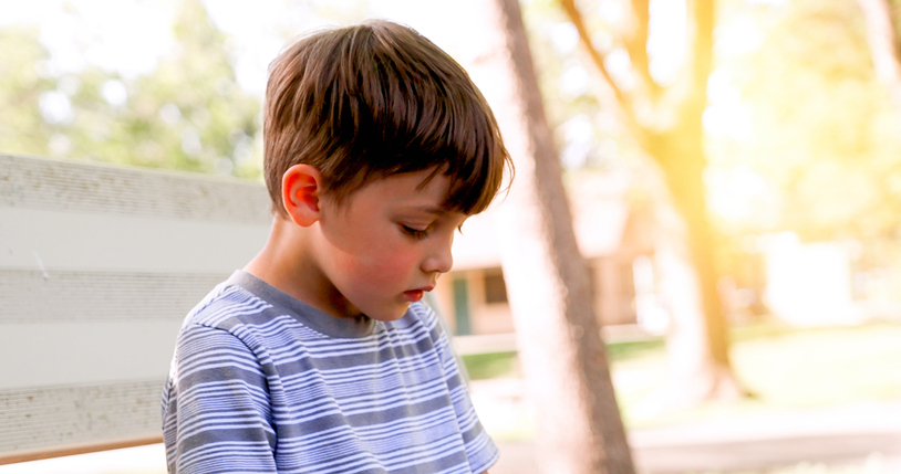 Sad, pensive, little boy looking down sitting at the schoolyard suffering bulling