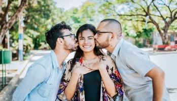 Two men kissing a girl cheek. Portrait of two guys kissing a girl cheek. Two young men kissing a woman cheek outdoor, love triangle concept. Polygamy concept