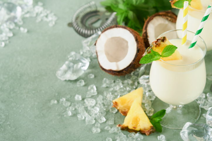 Pina Colada. Traditional caribbean cocktail from rum, pineapple juice and Coconut cream with tropical fruits and bar tools on fresh green background. Summer tropical cocktail and relaxation concept.